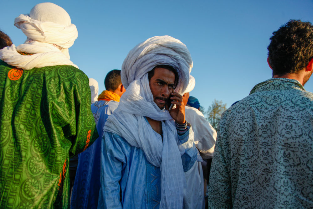 A festival attendee with gandoura, cheche, and cellphone.