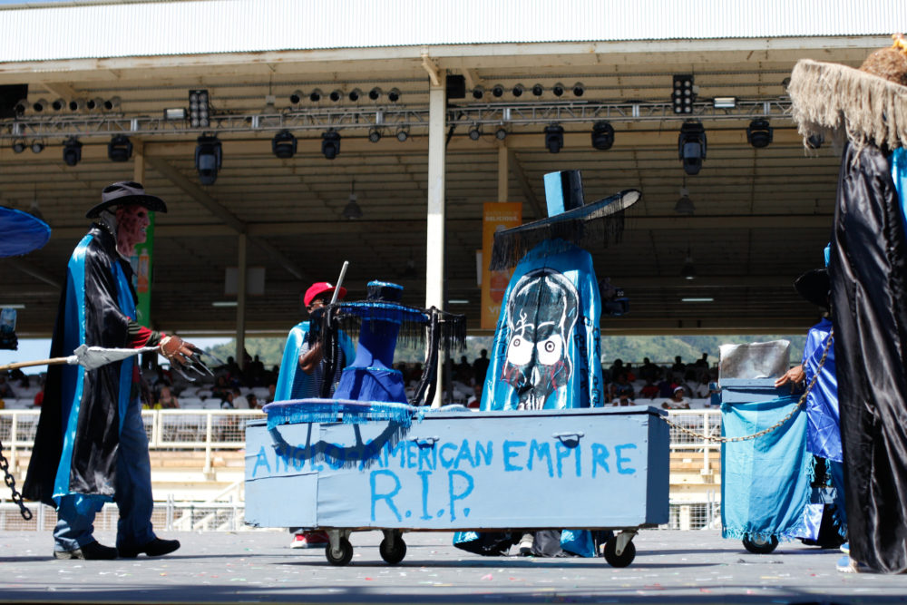 Part of a political commentary mas band, pulling a coffin that says "Anglo-American Empire R.I.P. "